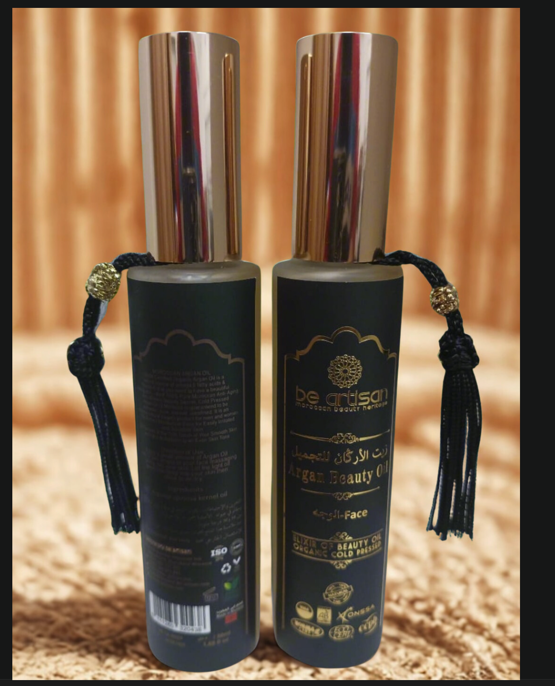 “Be Artisan Argan Beauty Oil in black and gold bottle with tassel, front and back view, premium skincare product on soft beige background.”