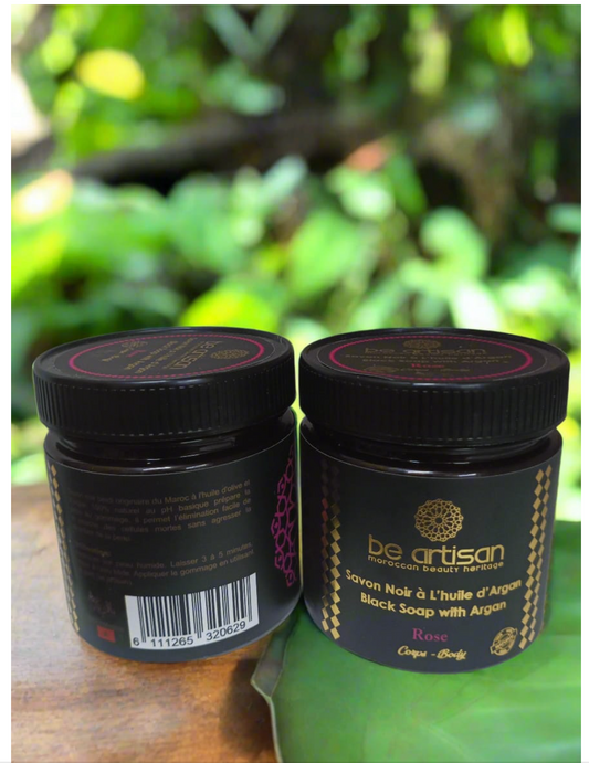 “Be Artisan Rose & Argan Black Soap jars on natural greenery background, traditional Moroccan black soap with rose fragrance.”