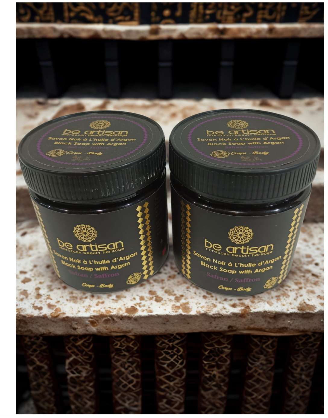 “Be Artisan Saffron & Argan Black Soap jars displayed on Moroccan decor, natural exfoliating black soap with saffron.”